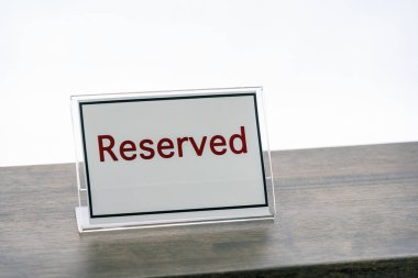 Ahşap masaya koyu kırmızı metin ile ayrılmış bir tabela yerleştirilir, bu da mekanın belirli bir amaç veya kişi için ayrıldığını gösterir. İşaret basit ve net.