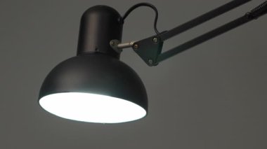 Siyah masa lambasını kapatan bir el, metal kollu modern ayarlanabilir aydınlatma armatürünü kapatan aydınlatmalı minimalist ofis çalışma alanı, çağdaş tasarım, sakin atmosfer, odaklı el.