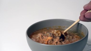 Hazır erişte çorbasını sıcak buharla karıştıran bir çubuk yemek, baharatlı Asya mutfağı konfor yemeği, hızlı yemek, basit öğle yemeği, lezzetli ve rahat bir atmosfer, dumanı tüten bir kase.