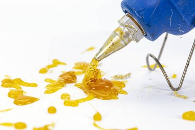 Beyaz yüzeye sarı yapışkan eriten mavi bir tutkal tabancası desenli desen oluşturuyor. Yapıştırıcı parlak ve canlı görünür, başlıktan yayılan ipliklerle, yaratıcılığı ve zanaatı gösterir