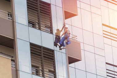 Erkek bir endüstriyel tırmanıcı, günışığında uzun ve modern bir gökdelenin camlarını yıkıyor.