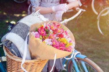Bir kadın retro bisikletinin sepetinde güzel bir buket ve battaniye