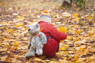 Sonbahar parkında ağaç yaprakları toplayıp toplayan bir çocuk.