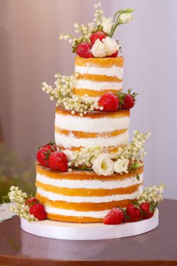 Üç katlı düğün pastası, süslü çilekler ve çiçekler.
