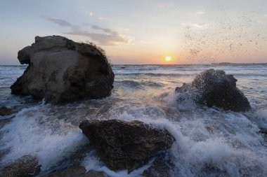 Gün batımında dalgalar plajda kayalara vuruyor. Kırım