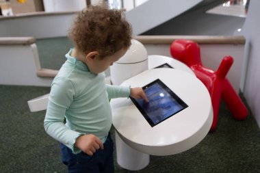 Çocuk bir oyun alanında eğitici bir uygulamayla meşgul oluyor. İnsanlar