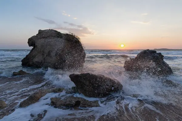 Gün batımında dalgalar plajda kayalara vuruyor. Kırım