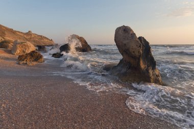 Gün batımında dalgalar plajda kayalara vuruyor. Kırım
