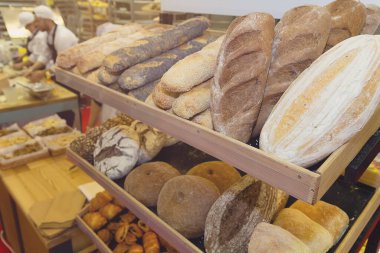 Sıcak bir fırının ahşap raflarında sergilenen taze pişmiş ekmek çeşitleri. Yiyecek.