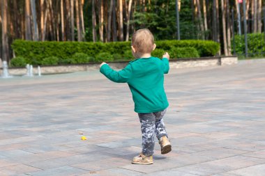 Bir çocuk parkta yürümeyi öğrenir. İnsanlar