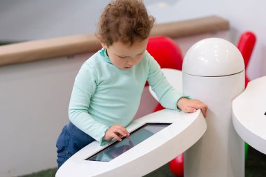 Çocuk bir oyun alanında eğitici bir uygulamayla meşgul oluyor. İnsanlar