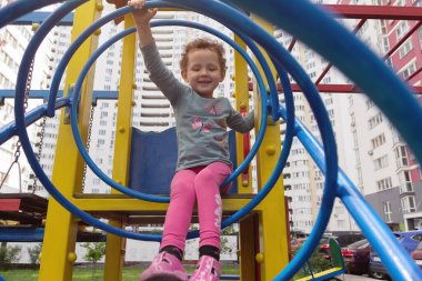 Kıvırcık çocuk çok katlı bir binanın arka planında oyun oynuyor. İnsanlar