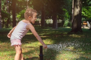 Küçük çocuk sıcak ve güneşli bir yaz günü bahçe hortumuyla oynuyor. İnsanlar