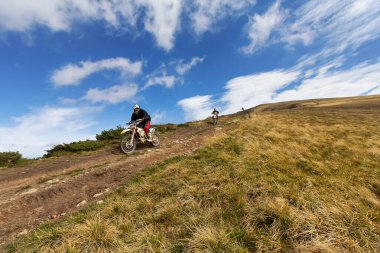 Enduro motorcusu dağlarda yüksek hızda karşıdan karşıya geçiyor. Karpatyalı