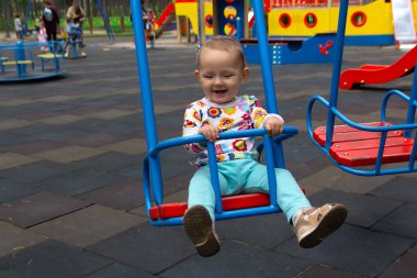 Bebek parktaki çocuk parkında salıncakta sallanıyor. İnsanlar