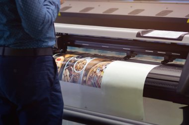 Endüstriyel baskı makinesi fabrikada renkli posterler basıyor. Matbaada üretim süreci, canlı renklerle yüksek hızlı yazdırma