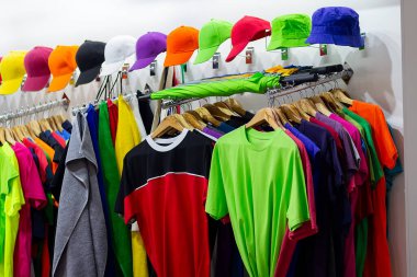 Bir spor mağazasının camında çok renkli tişörtler ve beyzbol şapkaları. Satılık.