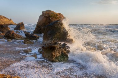 Gün batımında dalgalar plajda kayalara vuruyor. Kırım