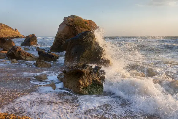 Gün batımında dalgalar plajda kayalara vuruyor. Kırım