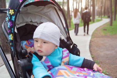 Çocuk, serin havada parkta yürüyüş yapmak için bebek arabasında. İnsanlar