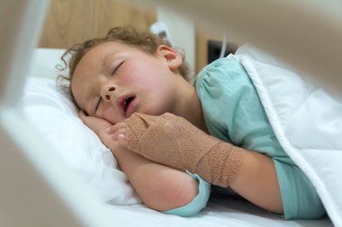 Küçük kıvırcık bir çocuk hastanede bir hastane yatağında uyuyor. İnsanlar