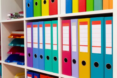 Modern ofis alanındaki bir rafta renkli klasörler. İşletmeler
