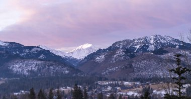 Winter landscape of mountain peaks and valley with houses at sunrise. clipart