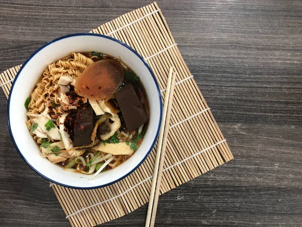 stock image Noodles in a white bowl. On bamboo background. Dark brown table. There are ready-to-eat side dishes in the cup