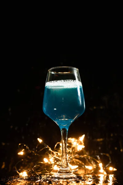 ワイングラス水があり 青い飲み物が動いています ガラスの底にはオレンジ色のボケがあります 祭りを祝うために招待し — ストック写真