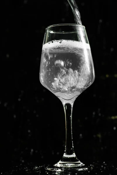 ワイングラス澄んだ水の飲み物が動いています 背景は黒 — ストック写真