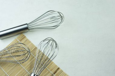 Tahta tezgahta ince beyaza konmuş çırpı çırpıcı. Arka planda düz olmayan beyaz alçı var.