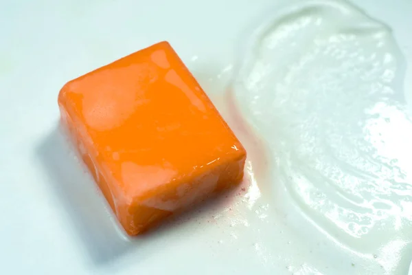 Orange soap, square shape, on a white sponge that comes from the soap, on a white background