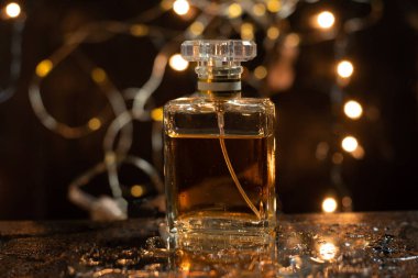 Siyah ıslak bir zeminde altın kahverengi dikdörtgen parfüm şişesi. Arkası turuncu bokeh.