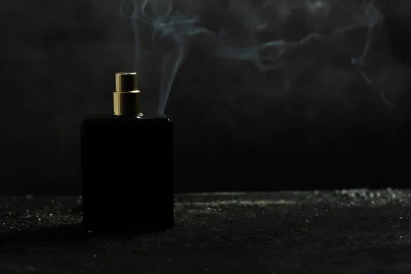 Siyah şişe parfümü. Arka tarafta duman var. Siyah bir arkaplanda
