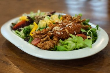 A large vegetable salad with battered fried crab in a white plate on the dining table, eat together to add balance in the body by eating vegetables