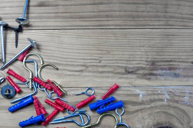 Duvara asılı şeyler için kancalar, yan tarafında plastik çapalar ve daha pek çok çeşit kanca var. Arkası bulanık kahverengi ahşap bir zemin.