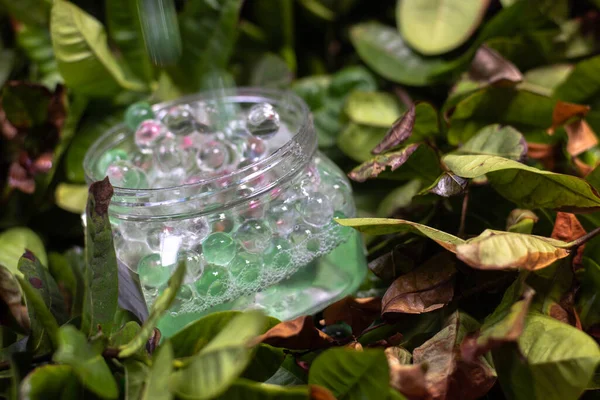 Air Freshener Crystal Beads, green, alternately clear and shiny, falling to each other. in motion on the ground of green leaves and dry, slightly brown