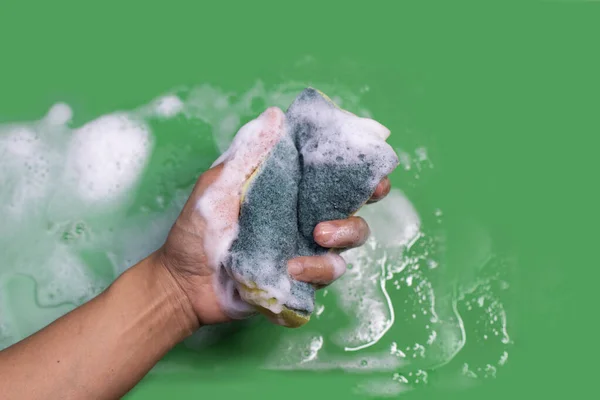 用绿色背景的盘子清洁剂手拿着发泡海绵 — 图库照片