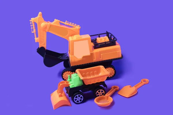 Orange toy backhoe and toy loader on a purple background