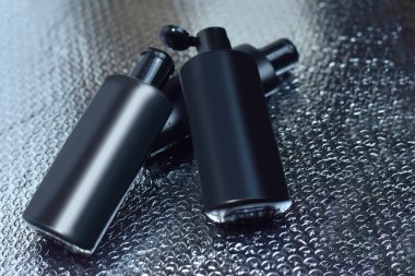 Siyah şişe, su damlalarıyla ıslanmış. Siyah arka planda hafif ıslak bir yansıma var. Ürün tanıtımı veya ambalajında kullanılabilir