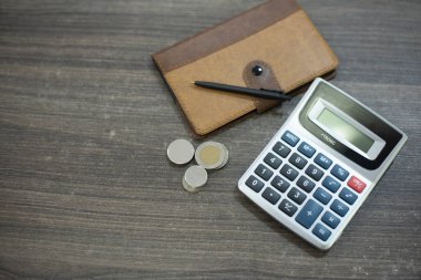 Not defteri, kahverengi kapaklı. Yanında hesap makinesi ve bozuk paralar vardı. Arka planda bir çalışma masası vardı. Kahverengi renk günlük hayattaki gelir ve giderleri hesaplamaya hazır ol. Bu, insanların göz ardı ettiği önemli bir konu.