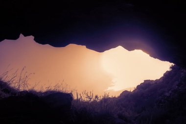 Turuncu bir günbatımı gökyüzünün olduğu bir mağarada taş bir delik.