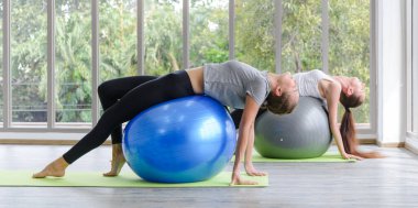 Egzersiz topuyla egzersiz yapan iki beyaz kadın. Fitness kızları spor salonunda karın kaslarını uygun topla esnetiyorlar.