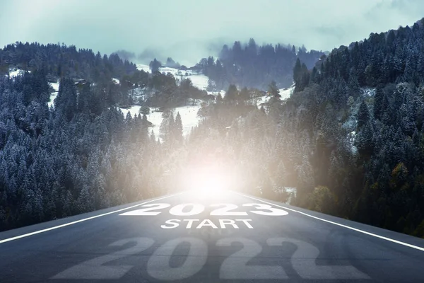 From the old Year 2022 start to the new year 2023 concept. Number of the old year 2022 and new year 2023 written on highway road in the middle of empty asphalt road through the pine forest