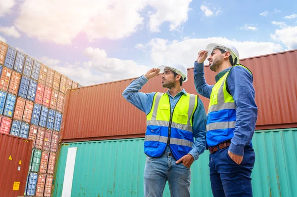Professional of two Engineers or foreman container cargo wearing white hardhat and safety vests checking stock into container for loading from Cargo freight ship for import export. industry worker of logistic concept