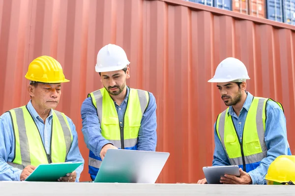 Group of container operators wearing helmets and safety vests meeting about logistics operations in container yards. Colleagues Talk About Logistics Operations