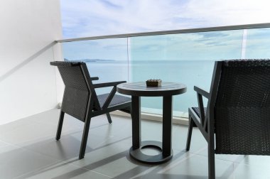 Mavi gökyüzünün altında deniz manzaralı kül tablası ve iki modern rattan koltuk. Seyahat balkonundan manzara. Yaz tatili kavramı. tatil yeri