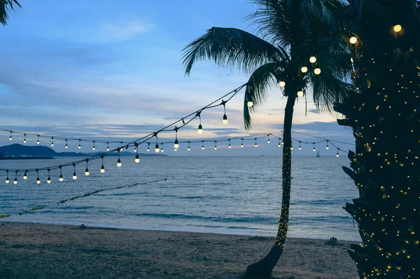 light bulbs on string wire decoration at the party event festival on the beach at sunset. Outdoor holiday background. Copy space