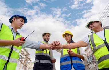 Group of contractors, engineers and formats in safety vests with helmets join hands to work together to successfully complete a construction project on construction site. cooperation and success concept