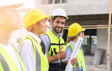 Group of contractors, engineers and formats in safety vests with helmets stand on the under-construction building site. teamwork concept